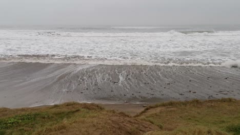 Día-Tormentoso,-Vientos-Fuertes-Y-Mareas,-Olas-Que-Se-Acercan-A-Una-Playa-Y-Un-Parche-De-Pasto-En-Las-Dunas-De-Arena