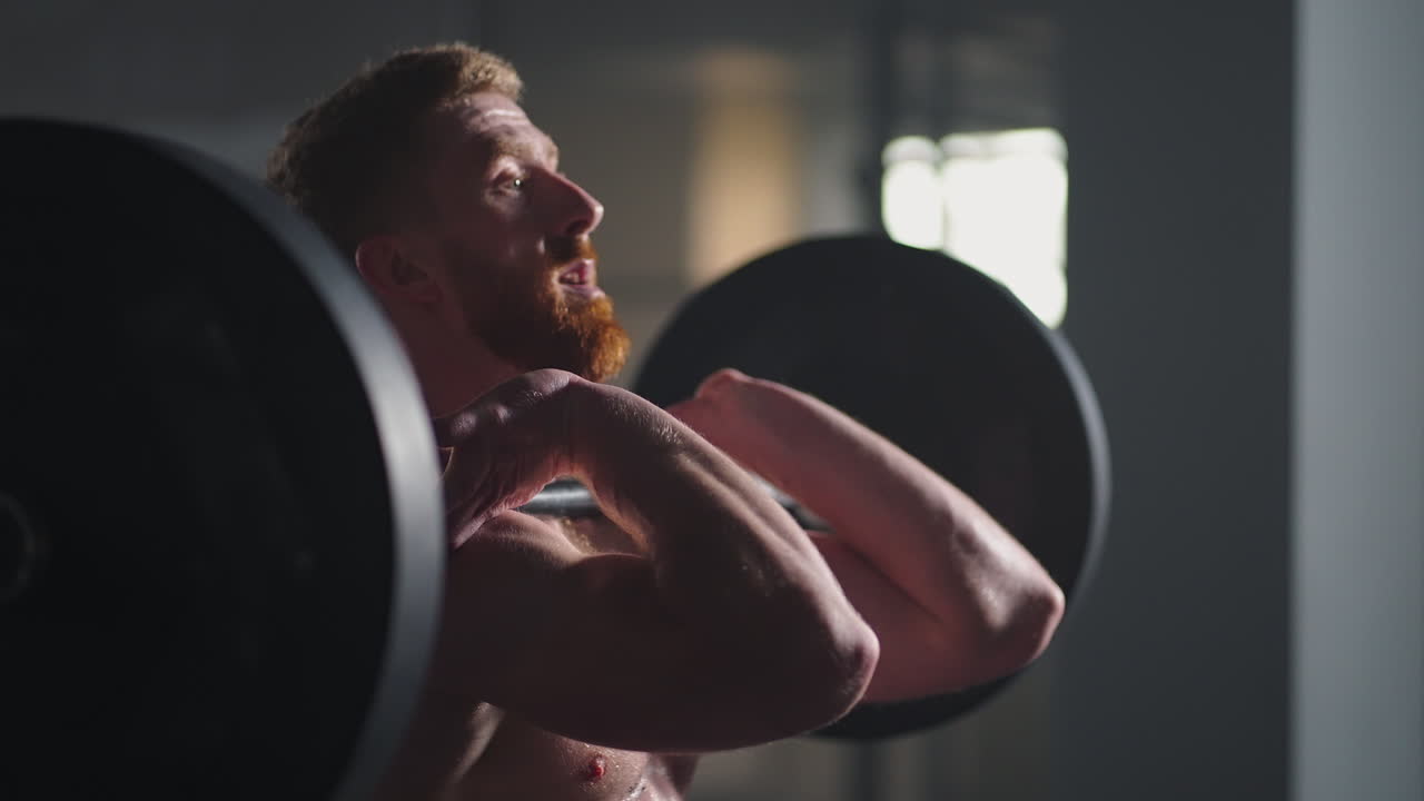 Un uomo atletico e di bell'aspetto esegue uno stacco da terra sopra la testa con bilanciere in palestra. Un magnifico bodybuilder professionista si allena con esercizi di sollevamento pesi in un'autentica struttura di allenamento fitness.