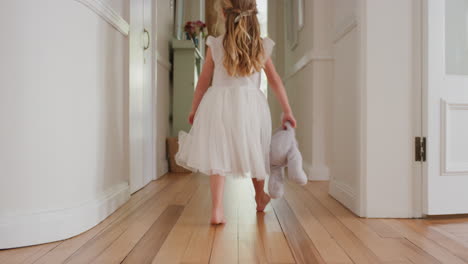 cute little girl walking through house holding teddy bear toy wearing pretty white dress rear view 4k