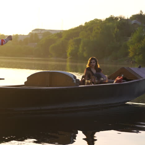 beautiful woman sitting in a boat and a man rowing by oar on the natural background at sunset.traditional venetian rowing boat with the gondolier and a female in the evening river.