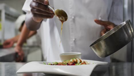 midsection of african american frmale chef garnishing dish in restaurant kitchen