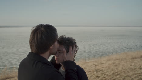couple sharing forehead kiss on romantic date near frozen lake