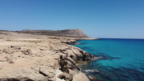 drone shot flying along a rugged coast surrounded by crystal clear blue water