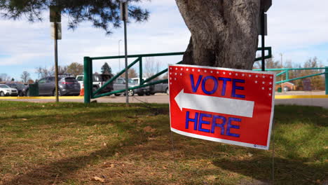 Vote-Here-Sign-Pointing-Left-with-Parking-Lot-and-People-in-Background