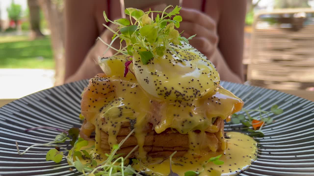 데친 달걀, 훈제 연어, 홀랜다이즈 소스를 곁들인 아보카도를 곁들인 맛있는 아침 브리오슈 토스트, 레스토랑에서 브런치를 즐기는 여성, 4k 샷