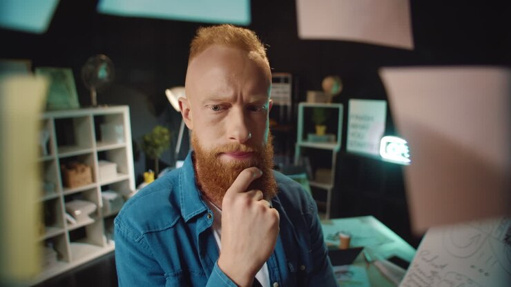 Giovane professionista hipster perplesso vicino a una bacheca di lavoro con post-it in ufficio.
