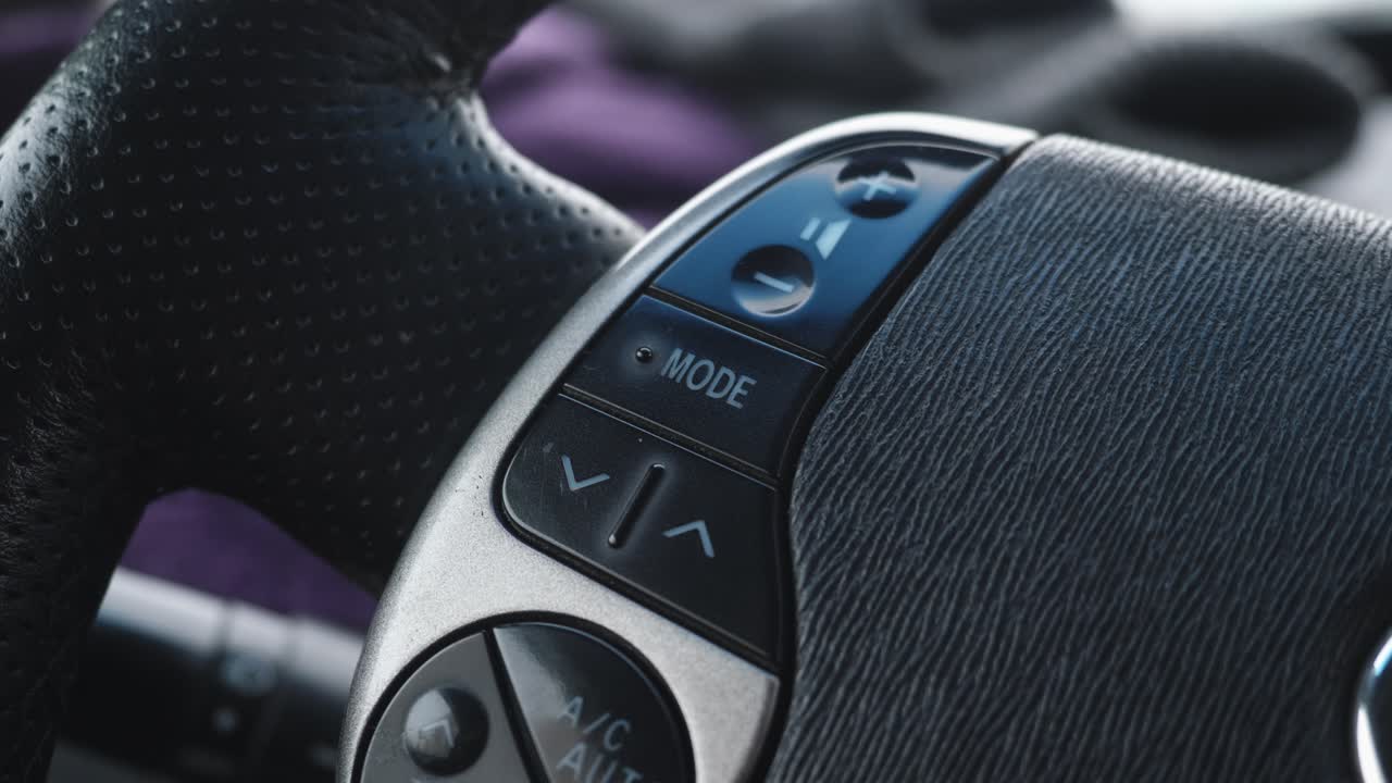 Detailed view of vehicle steering wheel controls. Focus on labeled buttons for functions like climate and system mode