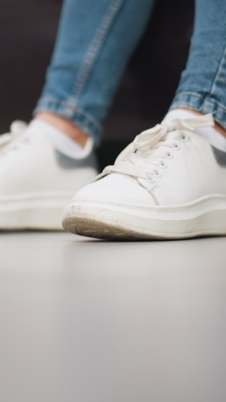 여성의  캔버스 스니커의 클로즈업은 편안한 쇼핑몰 설정에서 소파에 앉아있는 동안 청바지 바지와 함께 바닥에 왼쪽과 오른쪽 발을 부드럽게 합니다.