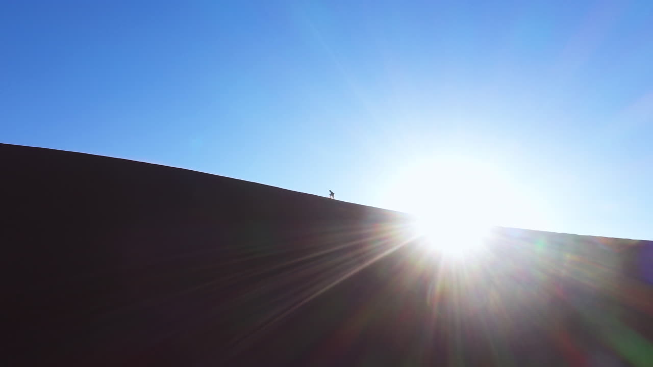 Aerial view around a man climbing on a sand dune, in sunny Namibia - low angle, circling, drone shot