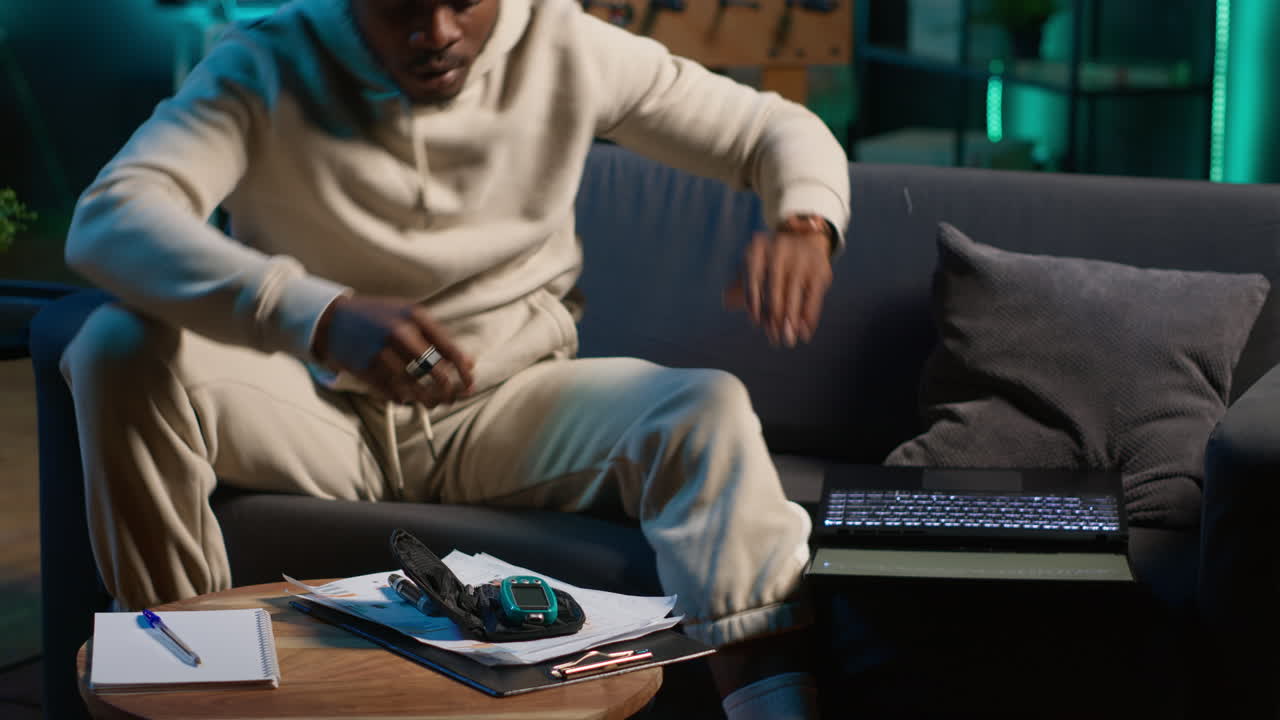 African american diabetic person working from home in his cozy apartment, using an insulin pen and measuring his glucose levels. Young adult with illness uses glucometer. Camera A.