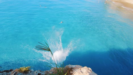 el joven hace una voltereta hacia atrás y aterriza de nuevo en un deslumbrante mar tropical mientras salta desde un acantilado