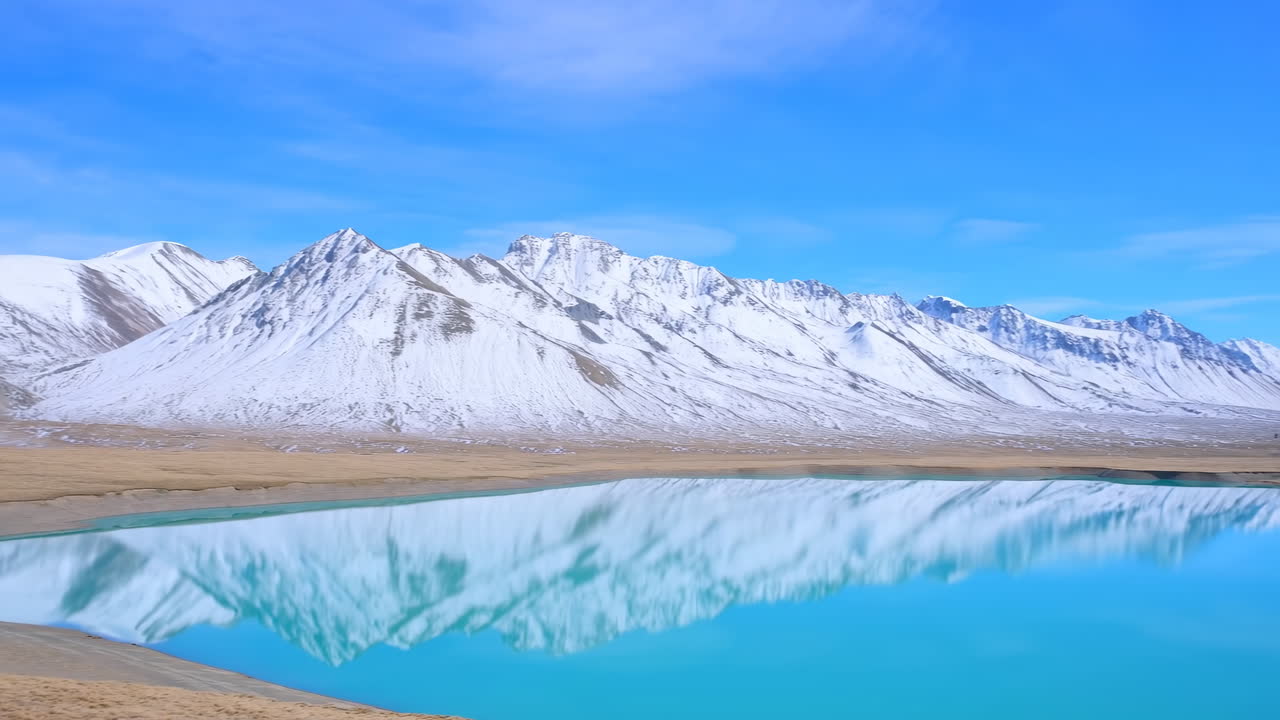 Turkos sjö som speglar snötäckta berg, filmatiskt drönarpanorama som fångar fridfull höghöjd
