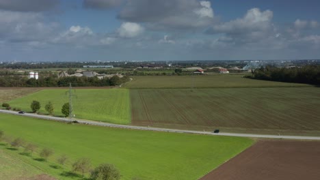 Aerial-view-over-a-rural-road-under-a-blue-summer-sky-with-the-cityscape-of-Munich-at-the-wide-horizon