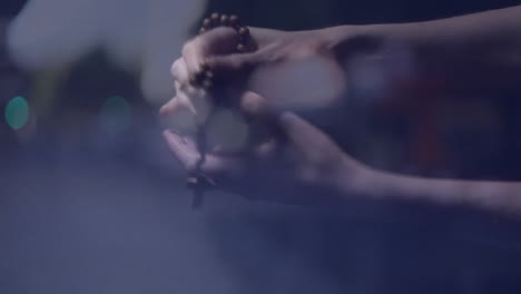 holding prayer beads, hands with blurred lights creating serene atmosphere