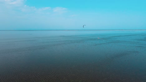 Una-Vista-Aérea-De-Un-Cuerpo-De-Agua-Con-Una-Persona-Practicando-Windsurf-Y-Parasailing,-Kitesurf-En-El-Océano-De-La-Laguna-De-Djerba-En-Túnez.