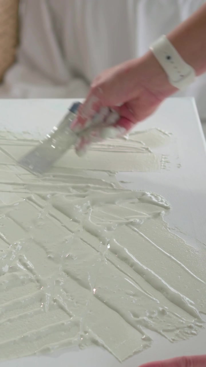 Vertical video: Artist scooping paste and spreading with palette knife, priming canvas for painting