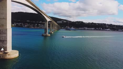 Aerial-View-of-Senja-Island-Bridge,-Norway,-Revealing-Drone-Shot-of-Boat-Sailing-Under-Modern-Crossing-on-Sunny-Summer-Day