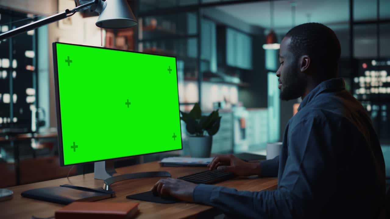 Handsome Black African American Specialist Working on Desktop Computer with Green Screen Mock Up Display at Home Living Room. Freelance Man Chatting to Clients Over the Internet on Social Networks.