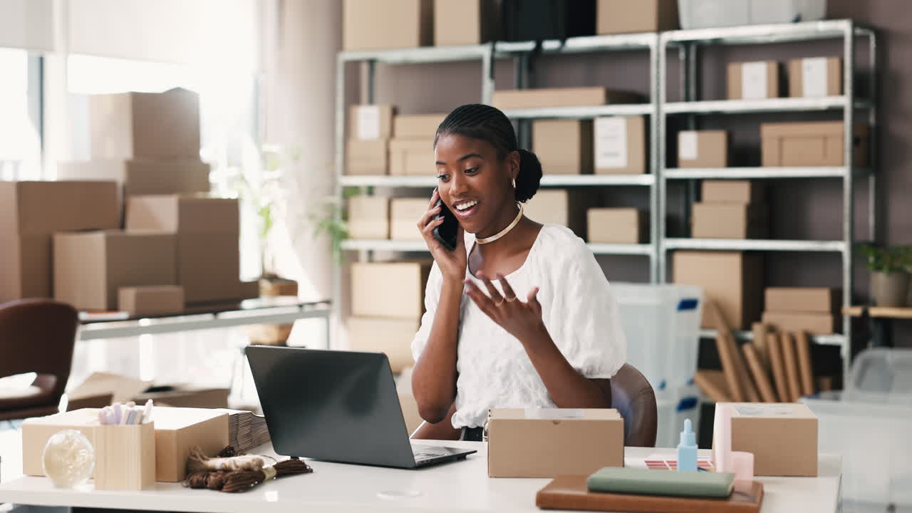 Giovane donna di colore parla al telefono e lavora al laptop in un ufficio e-commerce
