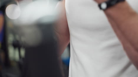 fitness expert in white singlet grips cable linkage, chest and arm contracting while pulling weight stack during focused strength workout inside modern gym, blurred equipment lights