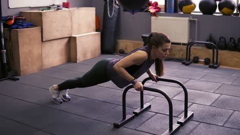 attractive sportive brunette girl doing push ups using push-up bars at the gym. working on strong arms and core. healthy lifestyle, fitness and wellbeing.