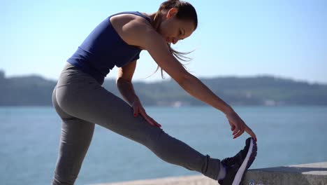 sporty young woman stretching leg at riverside