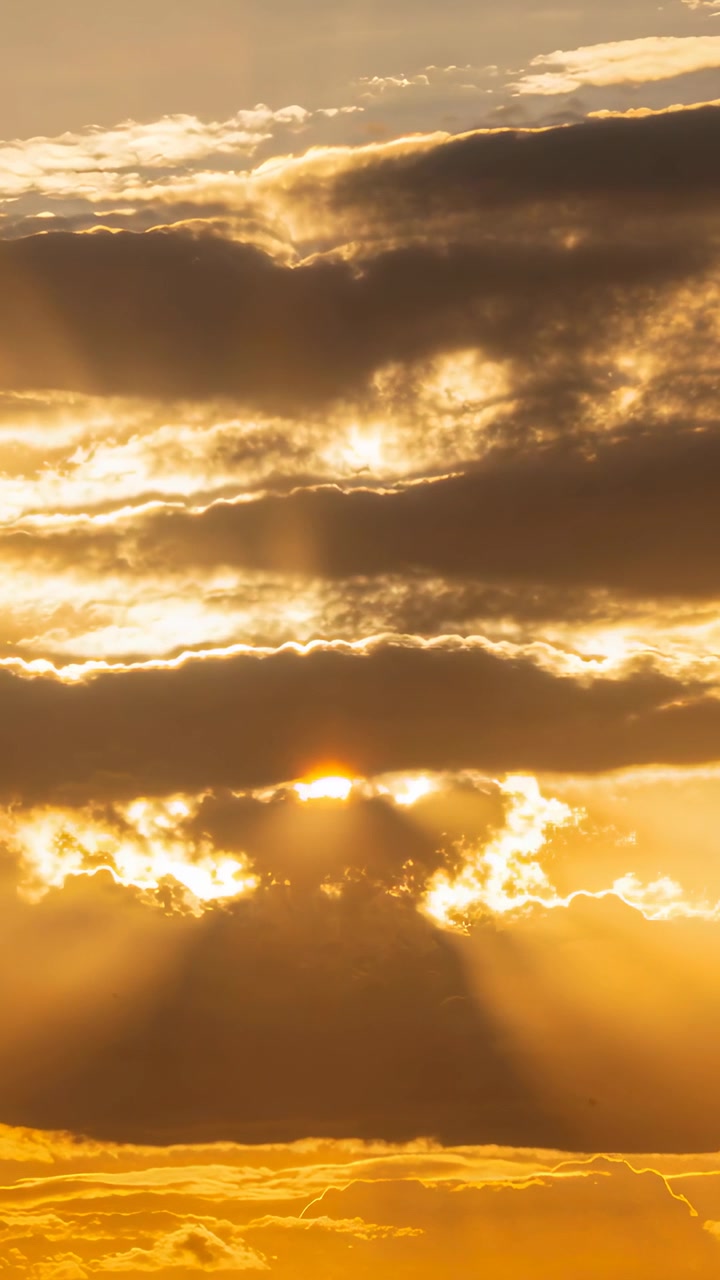 Vertical video: Peeking sun piercing gap opening at horizon, casting sun rays lighting gold edges