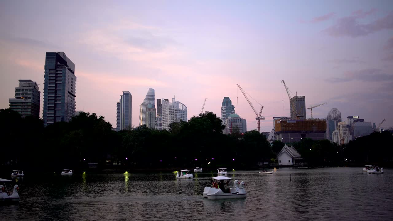 Lake in a park with catamarans in the background of skyscrapers and building cranes