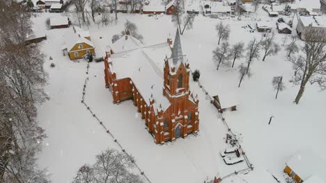 christmas season in small town with church during snowfall, aerial drone orbit view