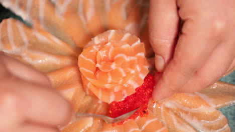 elegante presentación de sashimi - chef de sushi arreglando las finas lonchas de sashimi de salmón fresco en forma de flor con caviar rojo en un plato - disparo en ángulo alto