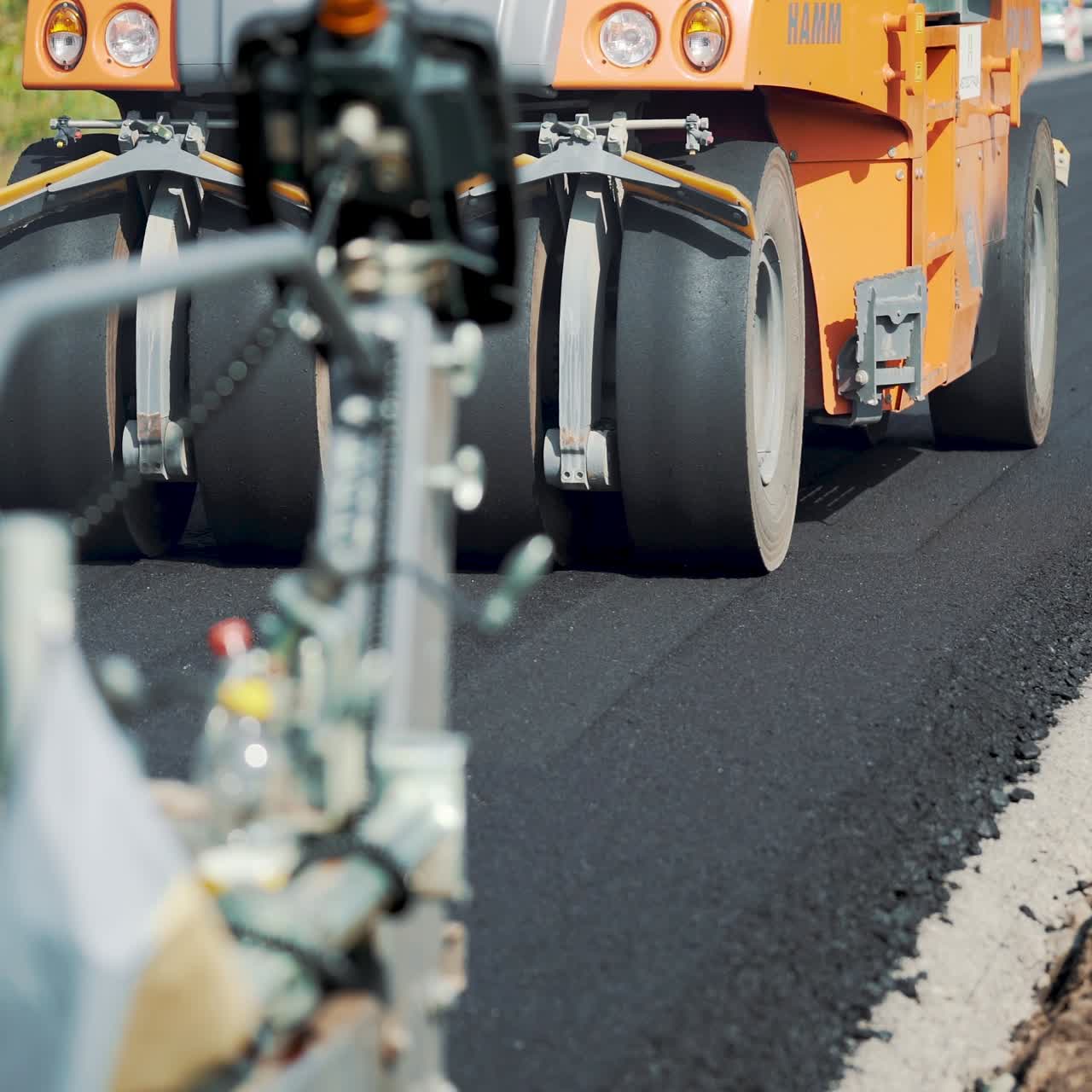 road machinery for leveling the ground passes the road under the supervision of workers. Close-up