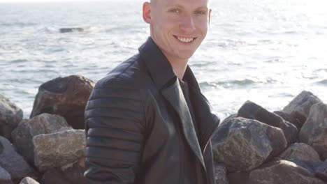 young man in leather jacket carries his longboard and smiles