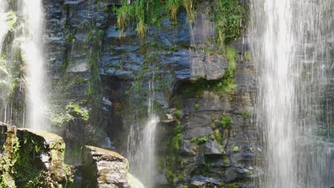 tilt down shot of waterfall crashing down rocky wall during sunlight in kerikeri waterfalls