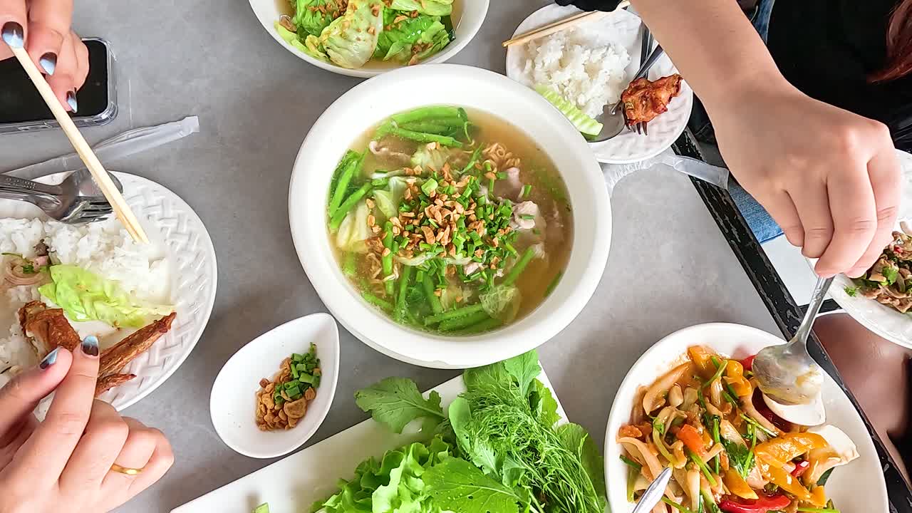 Overhead view of hands preparing and enjoying a traditional Lao meal with fresh ingredients and vibrant colors