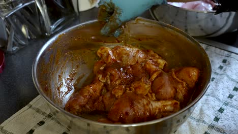 a chef, wearing gloves, expertly marinates chicken with sauce, and spices