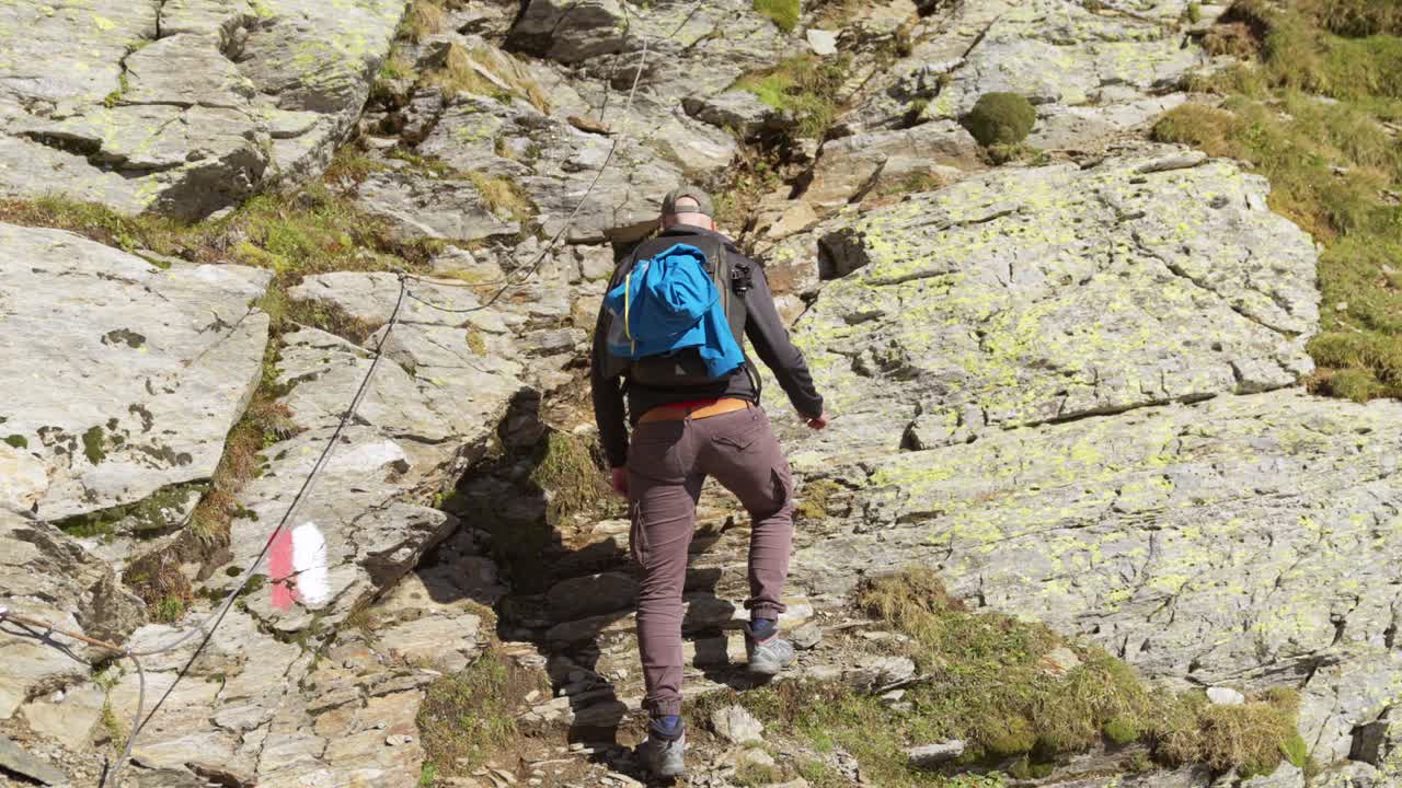 excursionista masculino en solitario escalando cuidadosamente la pared de roca usando una cuerda guía unida al muro de roca