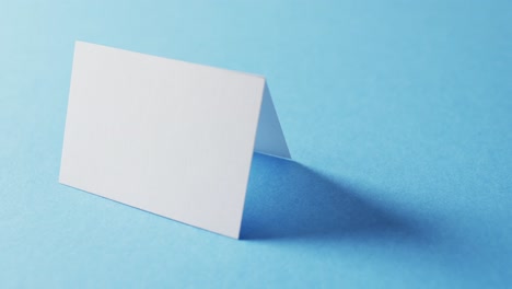 close up of two blank white business cards on blue background, copy space, slow motion