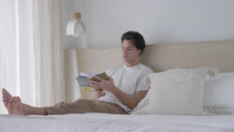 Hombre-Leyendo-Un-Libro-Mientras-Se-Sienta-En-La-Cama-Dentro-De-La-Habitación-Acogedora-Y-Tranquila