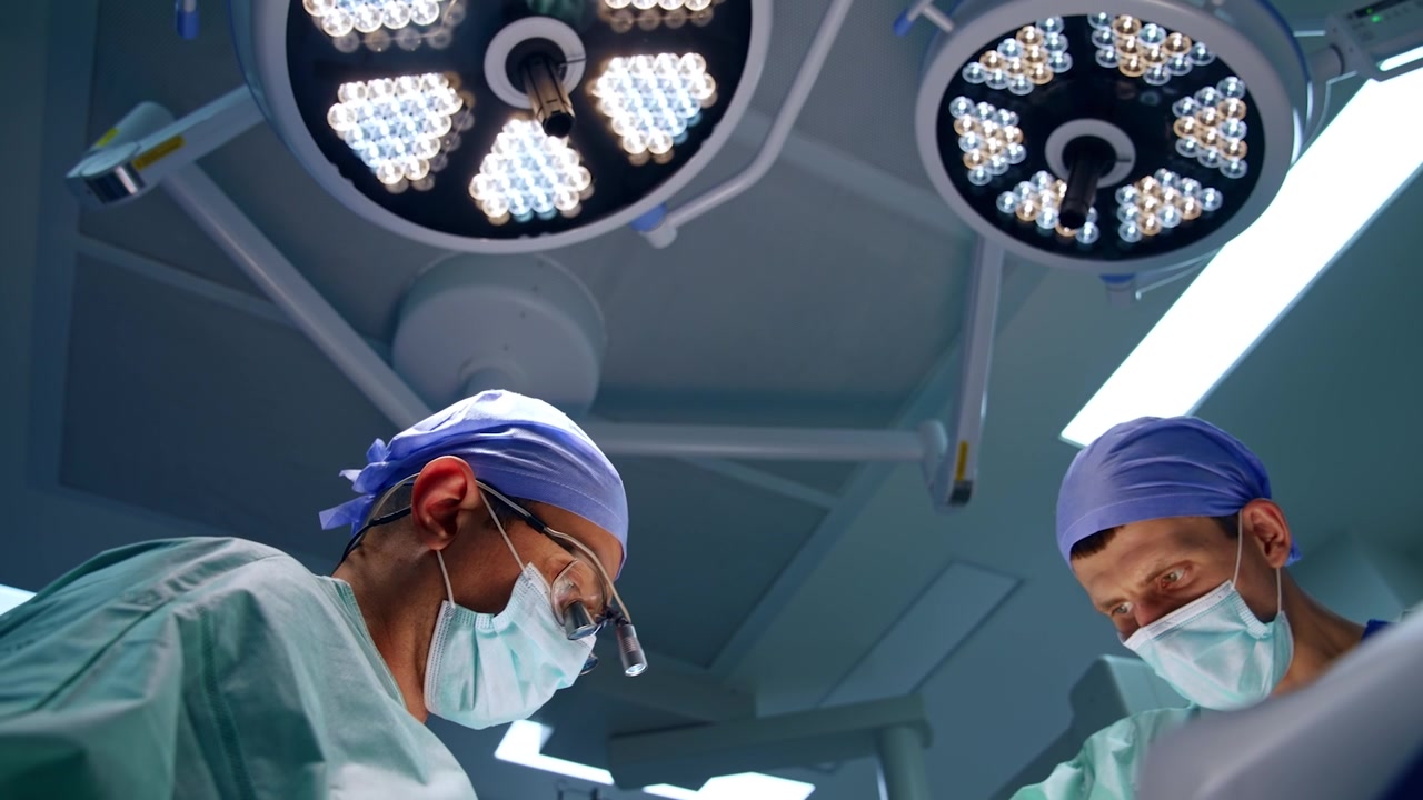 Medici lavorano durante un'operazione in una moderna sala operatoria. Lampade rotonde accese sul soffitto sullo sfondo. Inquadratura dal basso