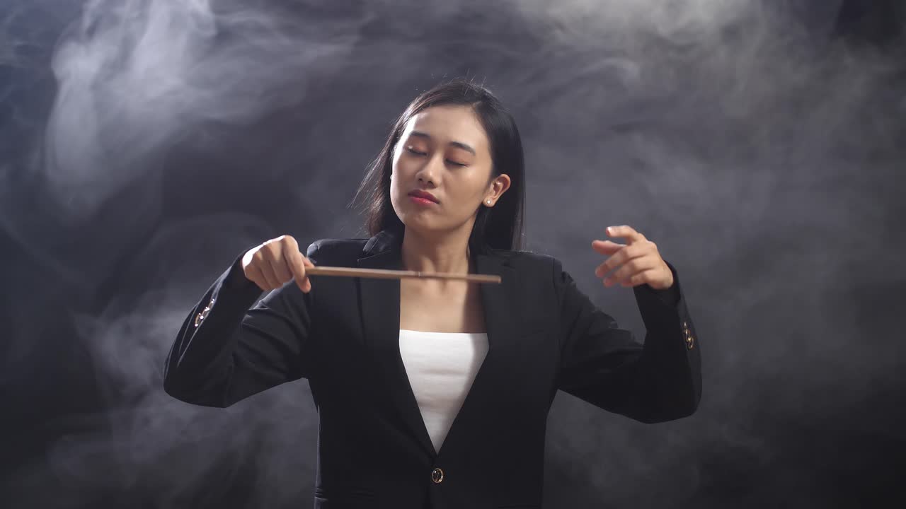 안개와 함께 검은 스튜디오에서 빨리 제스처를 보여주는 아시안 지휘자 여성