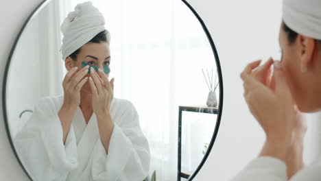 mujer aplicando parches en los ojos frente a un espejo