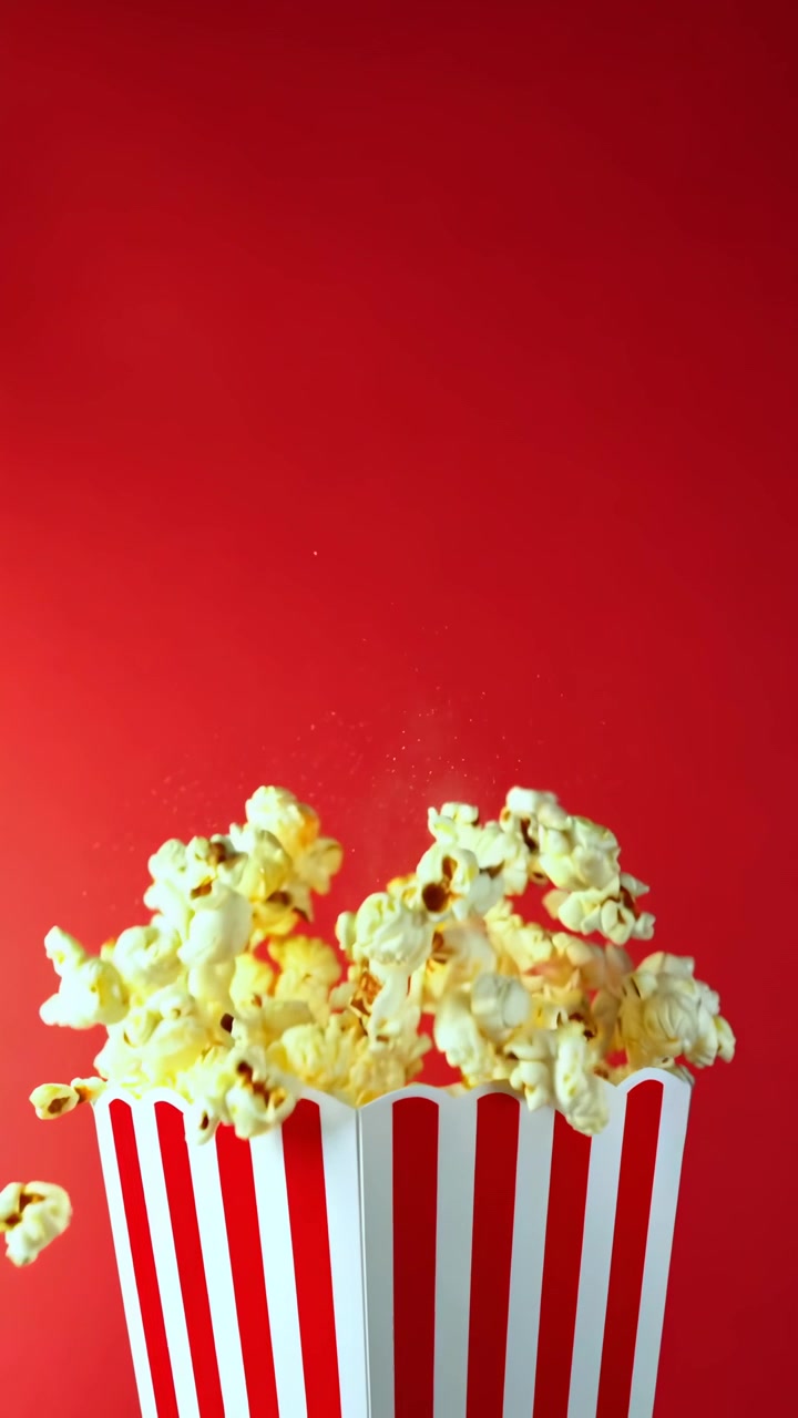 Popcorn che volano fuori da un secchiello a strisce su uno sfondo rosso