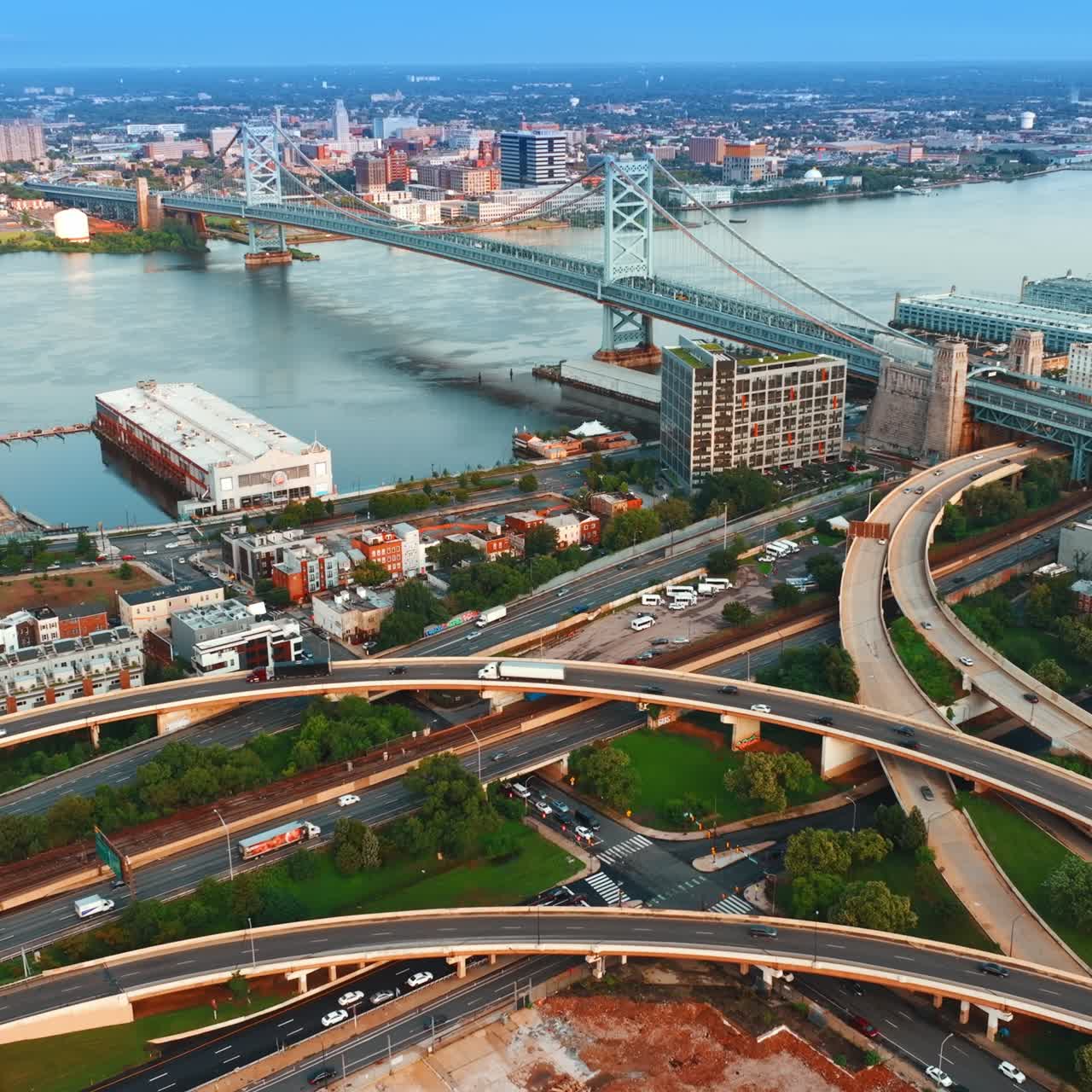 Transport going by the intertwining highways at waterfront of Delaware River in Philadelphia. The Benjamin Franklin Bridge at backdrop. Top view