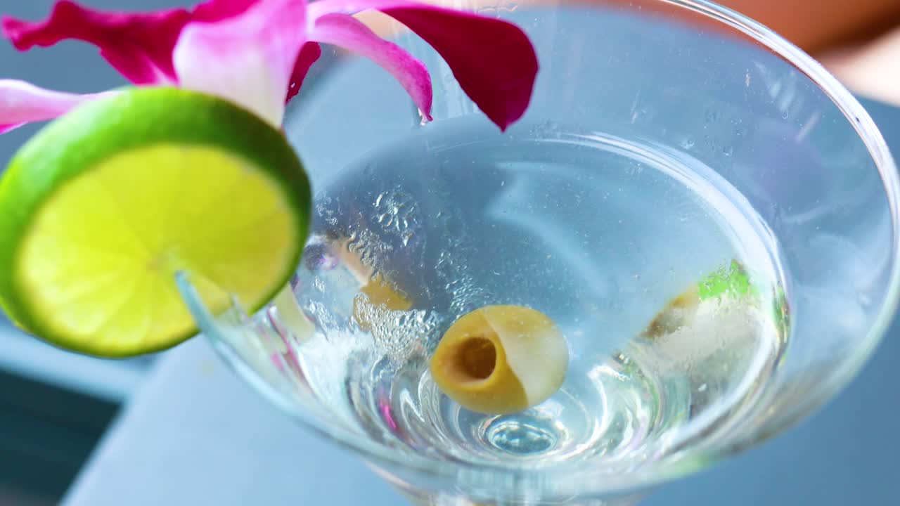 un vibrante martini de aceituna adornado con lima y orquídea, mostrando una presentación de cóctel refrescante en una iluminación brillante