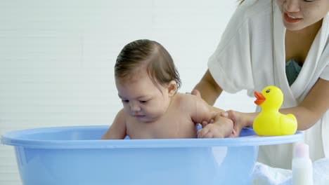 hygienic procedures for newborn, mother bathing her daughter in warm water, bathing the baby in the bathroom. newborn takes a bath in bathtub, baby girl smile happy face while take shower