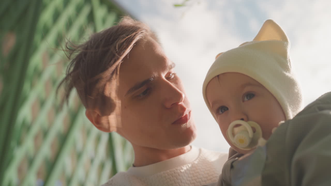Far krammer baby. Blid far trøster lille barn. Forælder holder kærligt et spædbarn udendørs. Udendørs omgivelser indfanger ømt øjeblik af far, der vugger sit spædbarn med kærlighed og omsorg.