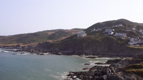 Aerial-Flyover-of-Rocky-Beach-in-North-Devon-with-Clifftop-Homes-in-Background