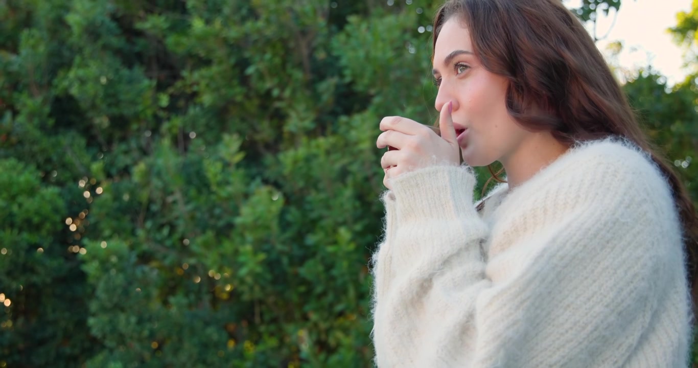 Donna appoggiata alla ringhiera di un balcone in vetro con un maglione bianco, che guarda e poi sorseggia da una tazza, spazio per il testo