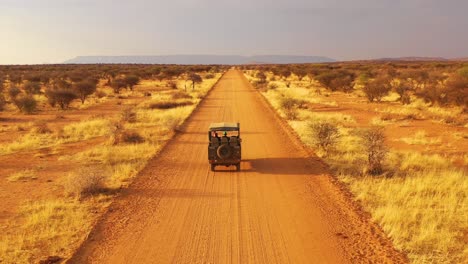 aerial of a safari jeep traveling on the plains of africa at erindi game preserve namibia with native san tribal spotter guide sitting on front spotting wildlife