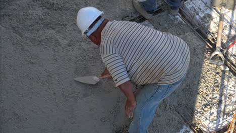 tiro inclinado hacia abajo de un trabajador de la construcción latino mexicano con un casco usando una paleta para aplanar el hormigón fresco en cámara lenta